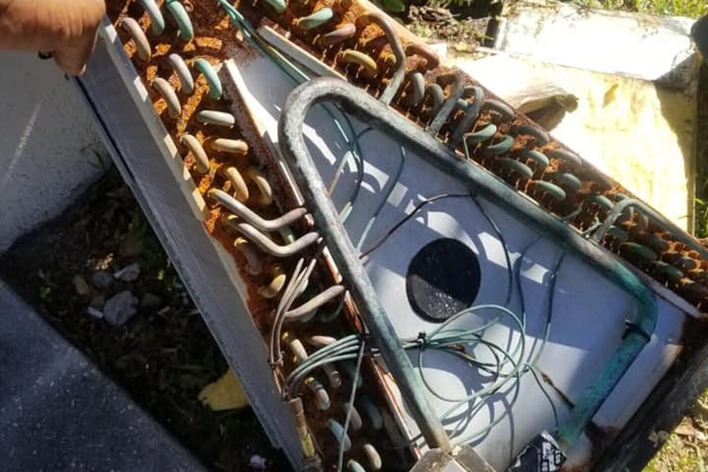 A coil removed from its cabinet and set on the ground, its tubing and fins heavily corroded.