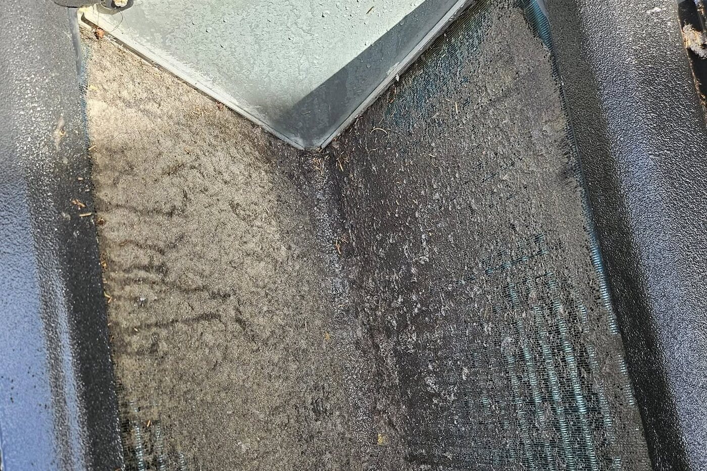 A close-up inside a unit, the pan and its screen buried under a thick mat of dust.