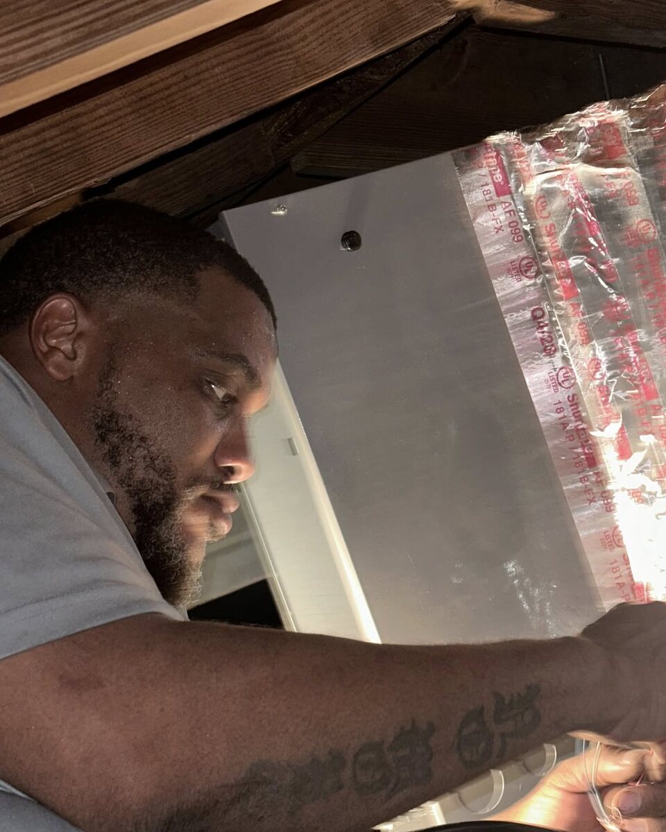 Quel Moragne working at a duct plenum inside a house, sealing a connection.